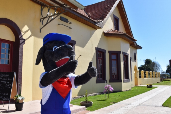 Cão Bilú, o mascote do município, concebido em parceria com projeto de extensão ligado ao Geoparque. Ao fundo, Estação Férrea (Foto: Comunicação/ Prefeitura de Restinga Sêca).